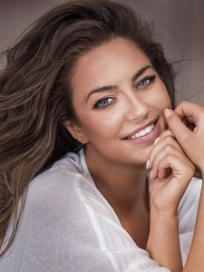 Woman with long brown hair smiling and gently touching her face, professional lifestyle portrait