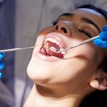 Dental professional in blue gloves performing dental procedure on patient with open mouth