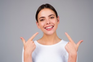 Happy young woman in white shirt smiling and pointing to her healthy teeth