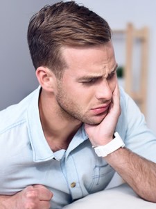 Young man in light blue shirt holding his jaw in pain, representing toothache or dental discomfort